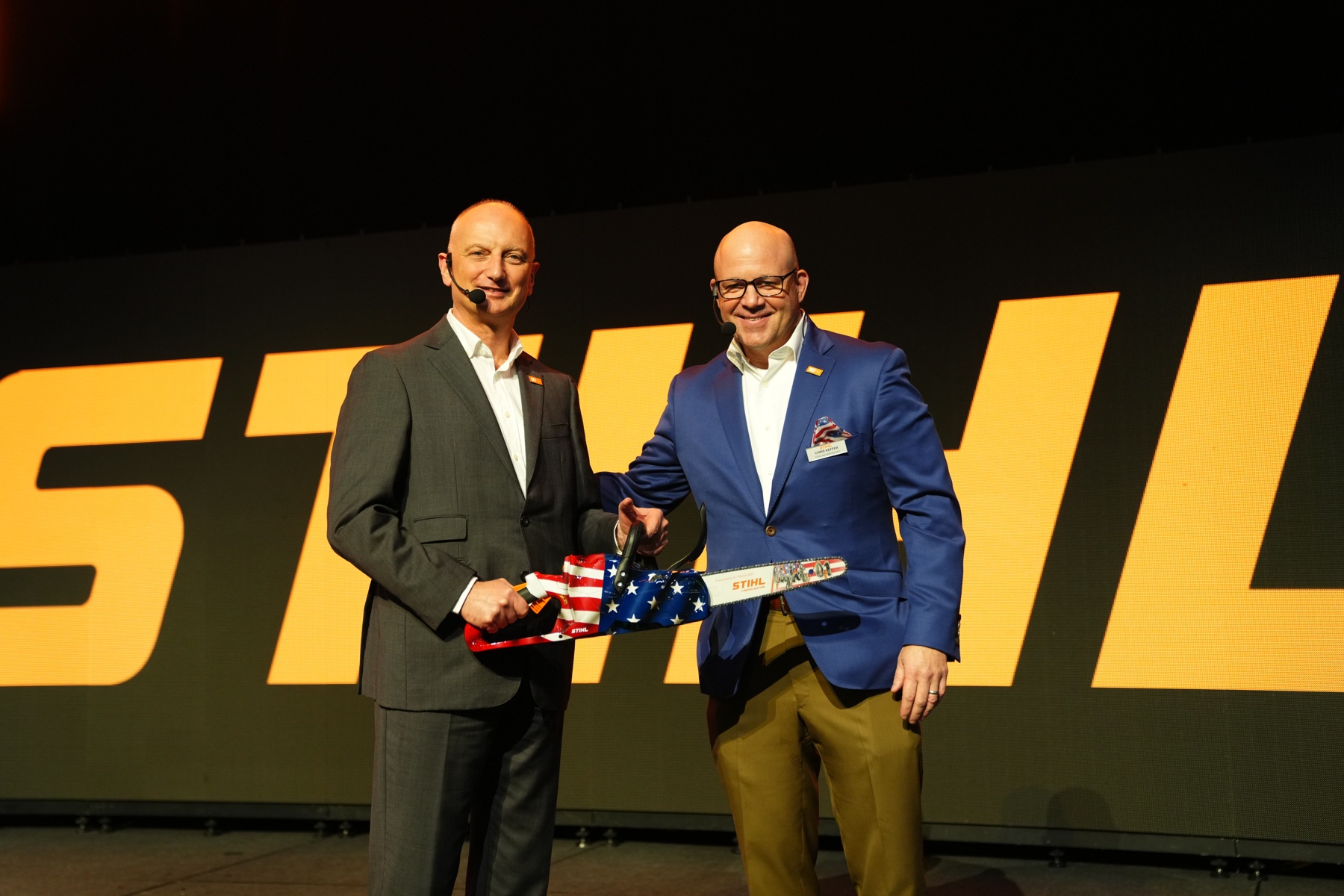 Dr. Nikolas Stihl (vänster) och Chris Keffer, VD för STIHL Inc. i USA, presenterar en jubileumssåg med en amerikansk flagga.